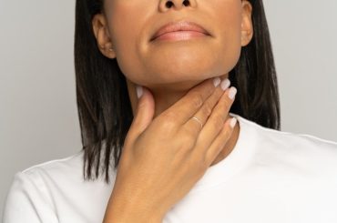A woman holding holding her hand up to her sore throat