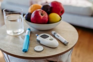 A glass of water, a bowl of fruit and personal Diabetes testing devices sit on a small round coffee table.