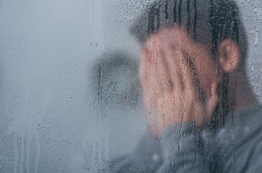 Raindrops on a window with a stressed man in the background with his hands over his face